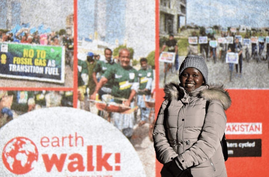 Person wrapped in grey jacket and hat infront of Earth walk banner