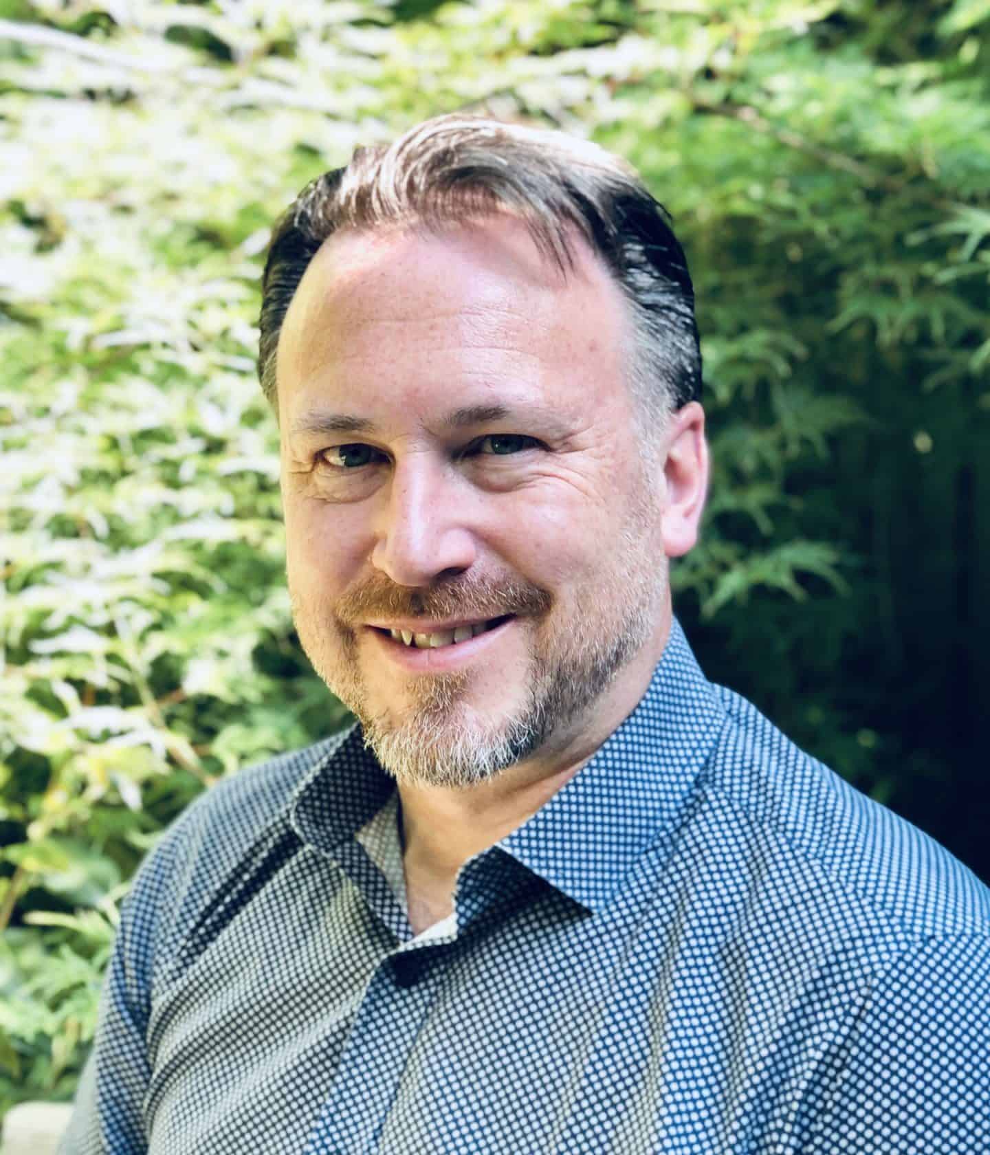 a man in a blue shirt smiles at the camera with a green background